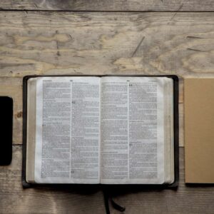 overhead shot of opened bible in the middle of a notebook and a smartphone on a wooden surface